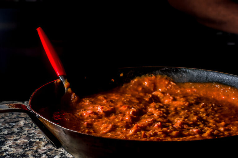 A close-up of a pan with simmering sauce and a red-handled spoon stirring it.