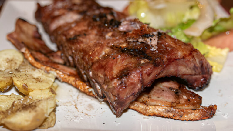 Close-up of grilled ribs served with sliced potatoes and lettuce