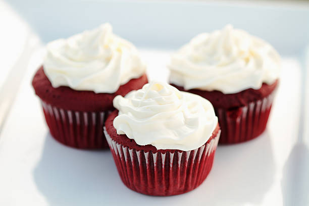 Three red velvet cupcakes with cream cheese frosting on a white plate.