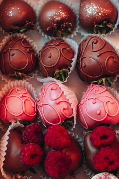 A selection of decorative chocolates shaped like strawberries, featuring dark and pink chocolate with intricate designs and fresh raspberries.