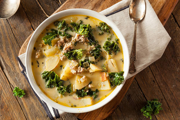 A bowl of hearty soup with kale, potatoes, and ground meat on a wooden surface