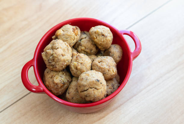 A red bowl filled with small, round cookies on a wooden surface.