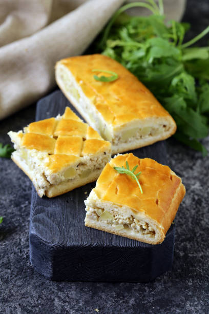 Savory baked pastry with a golden crust, filled with cheese, displayed on a dark wooden board alongside fresh herbs.