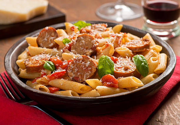 A delicious plate of penne pasta topped with sausage, tomatoes, basil, and grated cheese.