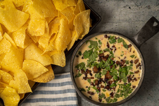 A bowl of creamy dip topped with chopped herbs and bacon bits next to a tray of tortilla chips.