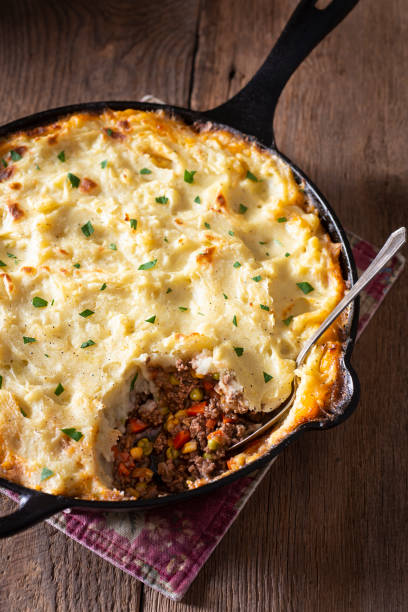 A cast iron skillet filled with shepherd's pie topped with golden mashed potatoes and garnished with parsley.