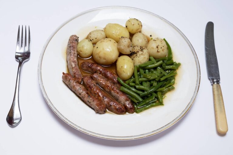 A plate of sausages, boiled potatoes, and green beans on a white background.