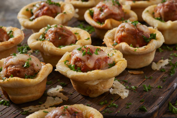 Mini meatball cups topped with cheese and parsley on a wooden surface.