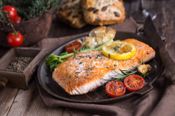 A beautifully cooked salmon fillet garnished with lemon and herbs, served on a rustic plate with roasted vegetables and cherry tomatoes.