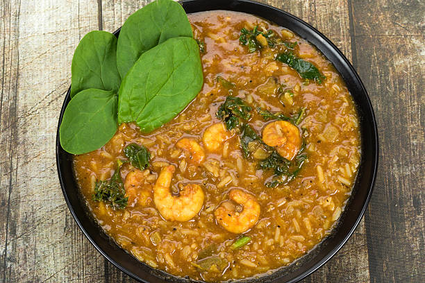 Bowl of shrimp and rice stew with spinach on a wooden surface