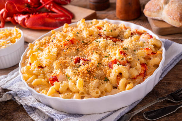 Baked macaroni and cheese with lobster in a white dish, garnished with breadcrumbs, served on a table with lobster and bread in the background.