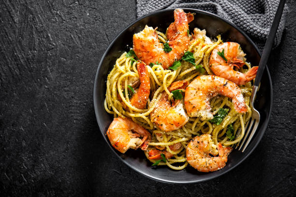 A close-up view of a black bowl filled with shrimp pasta, featuring large, juicy shrimp and spaghetti tossed with herbs.