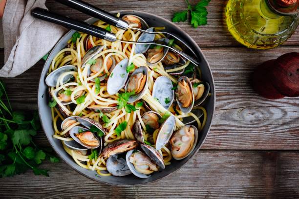 A bowl of spaghetti with clams and fresh herbs on a wooden table