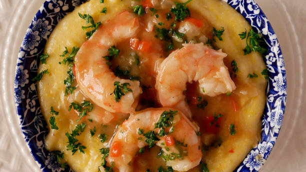 A dish of creamy grits topped with sautéed shrimp and garnished with parsley, served in a decorative blue and white bowl.