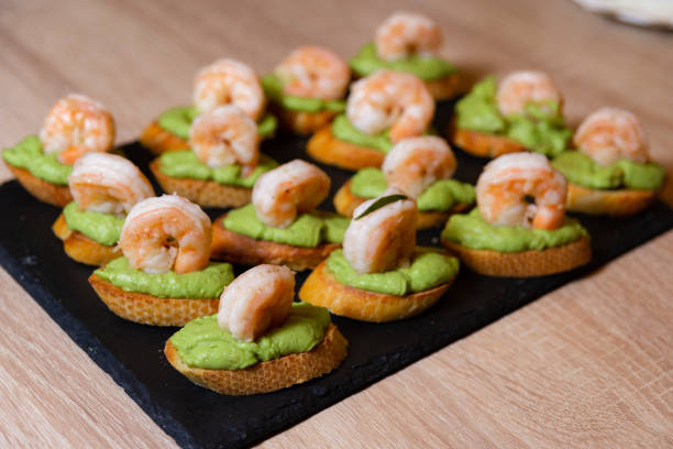 A platter of shrimp appetizers on toast with green spread.