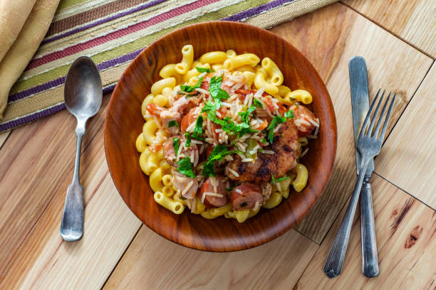 A bowl of macaroni pasta topped with chicken, sausage, and parsley, placed on a wooden table.