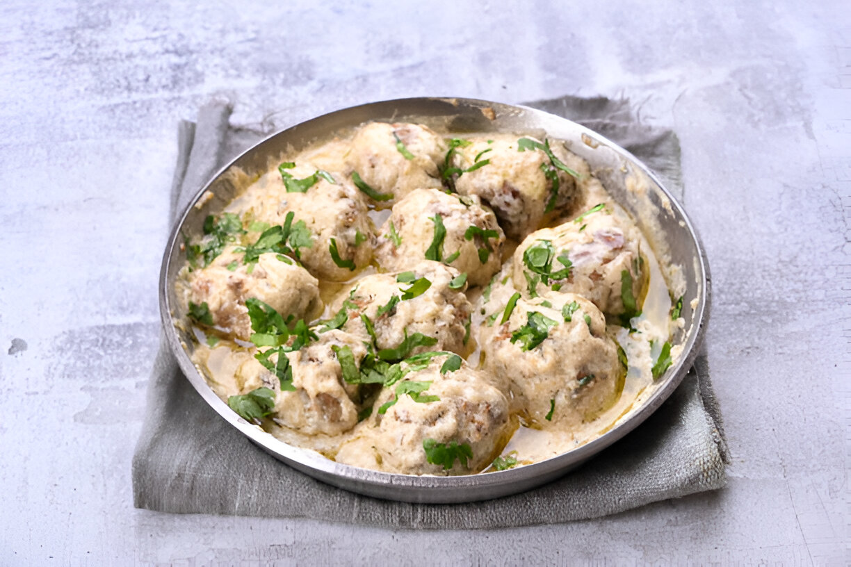 A round metal dish filled with creamy meatballs garnished with fresh cilantro.