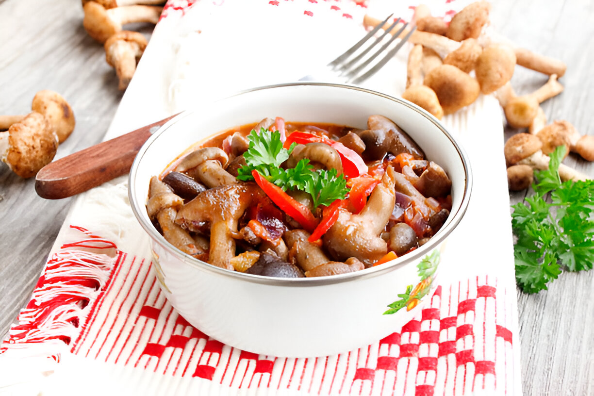 A bowl of mushroom stew garnished with cilantro and sliced red peppers, placed on a woven cloth with mushrooms in the background.