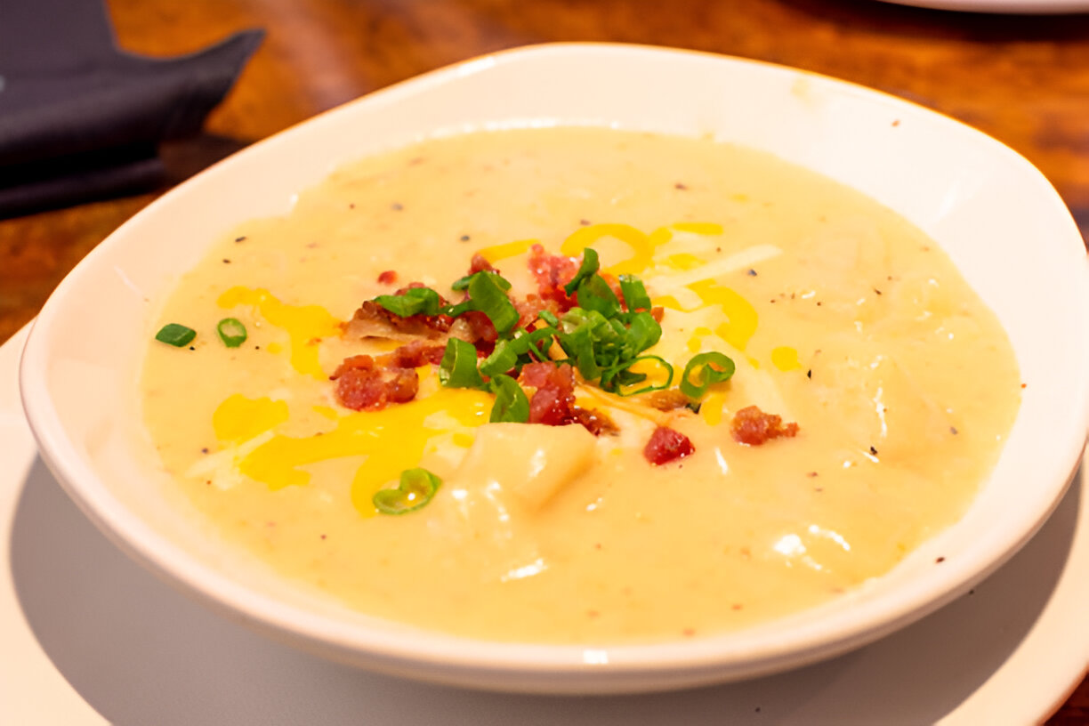 A bowl of creamy soup topped with chopped green onions, cheese, and bits of bacon.