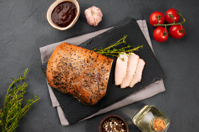 A beautifully arranged slate platter featuring sliced meat, fresh herbs, cherry tomatoes, and a small bowl of sauce.