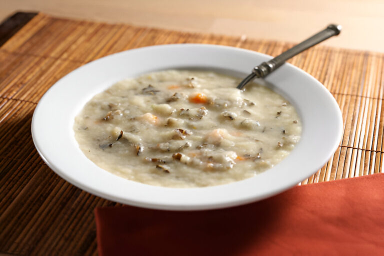 A bowl of creamy soup with small pieces of vegetables and herbs, placed on a bamboo mat