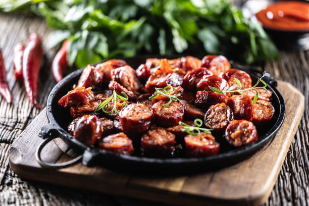 A sizzling platter of sliced sausage served with garnishes on a rustic wooden surface.