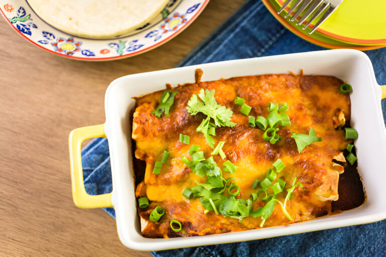 A close-up view of a yellow dish filled with cheesy enchiladas garnished with green onions and cilantro, placed on a blue cloth.