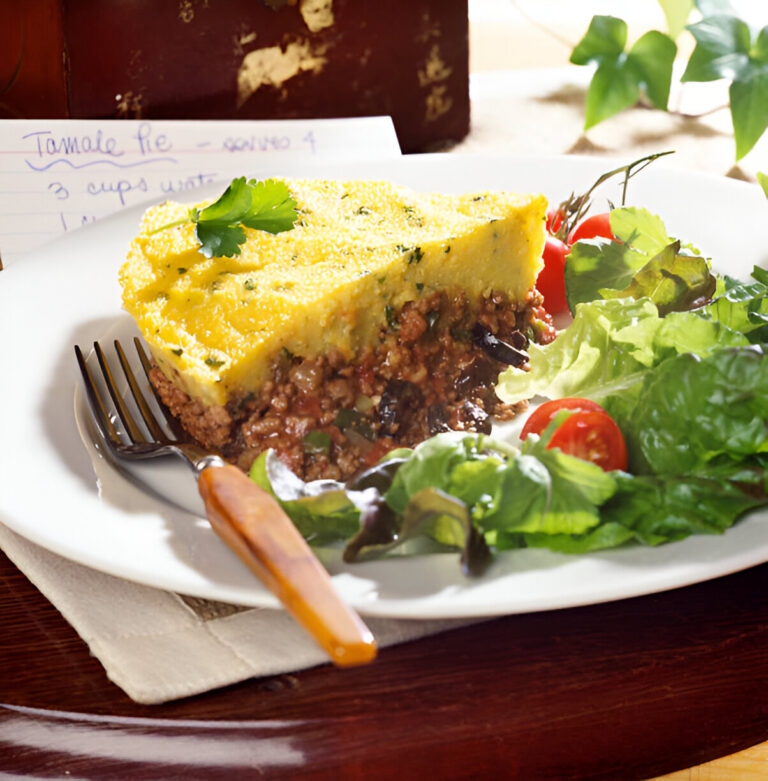 Slice of tamale pie served with fresh salad and cherry tomatoes on a white plate.