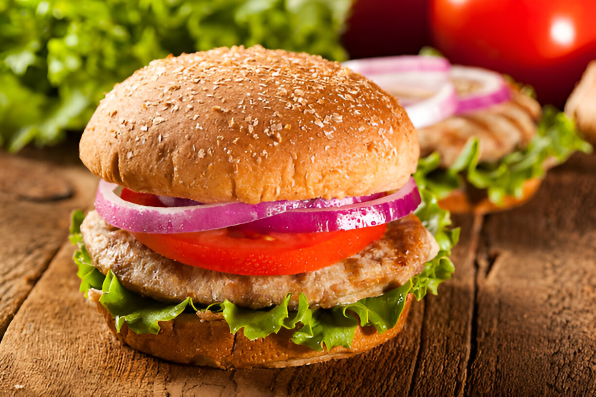 A close-up of a delicious burger with lettuce, tomato, red onion, and a sesame seed bun.