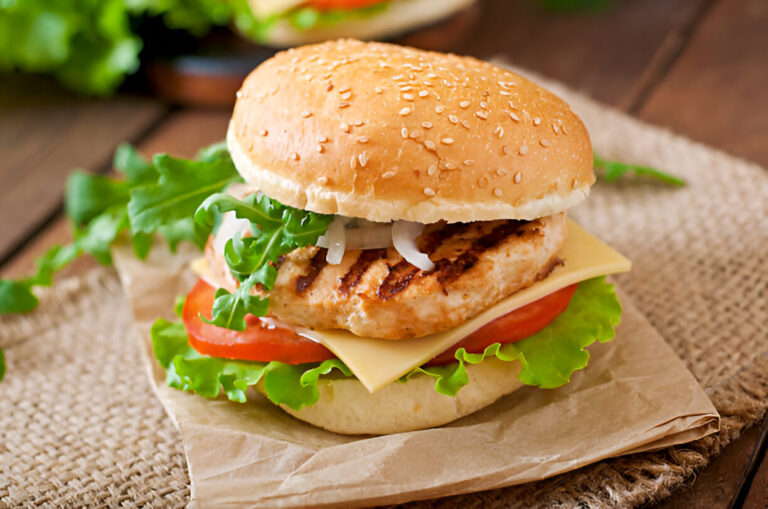 A delicious grilled chicken burger with lettuce, tomato, cheese, and onion served on a sesame seed bun.