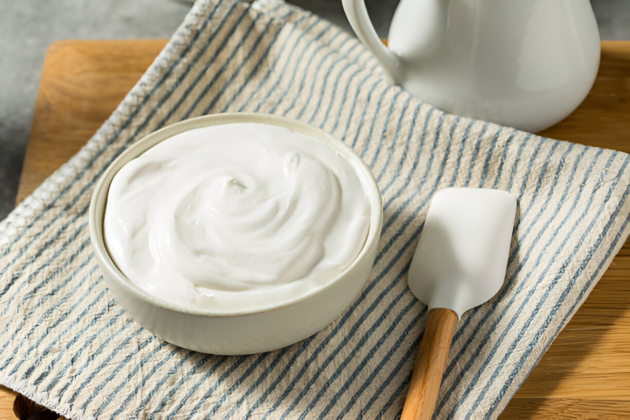 A bowl of creamy yogurt on a striped cloth with a spatula beside it