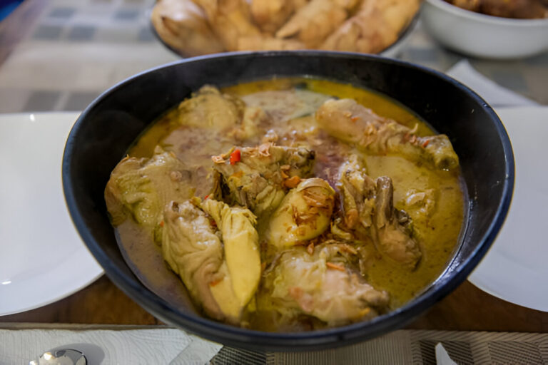 A bowl of delicious chicken curry with yellow sauce and garnished with herbs and spices.