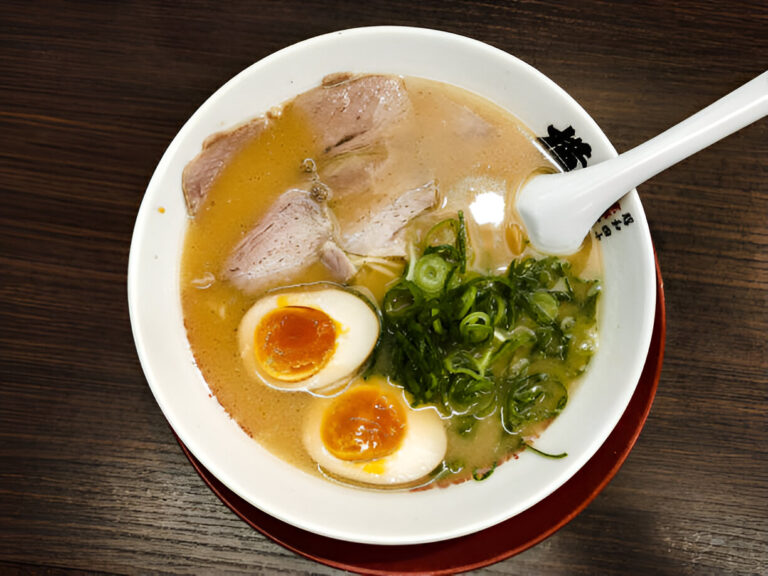 A bowl of ramen featuring sliced pork, soft-boiled eggs, green onions, and a rich broth.