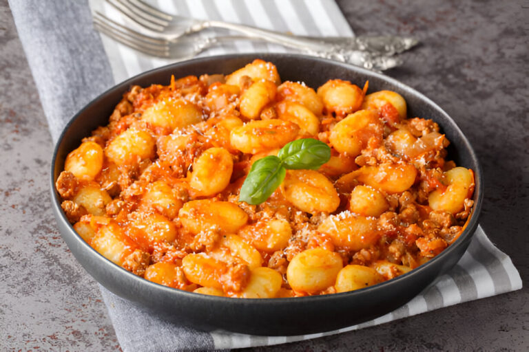 A delicious serving of gnocchi with meat sauce in a black bowl, garnished with fresh basil.