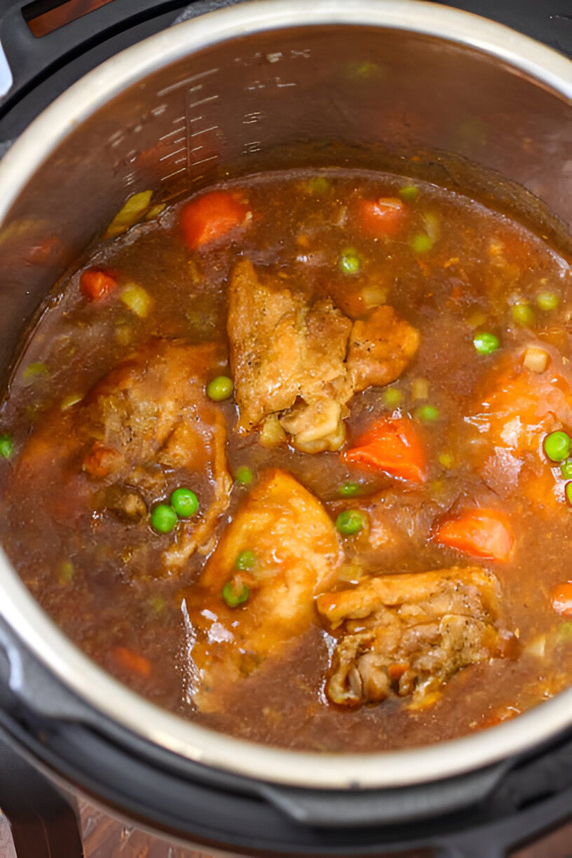 A steaming pot of chicken stew inside an Instant Pot, featuring chicken pieces, peas, carrots, and rich broth.