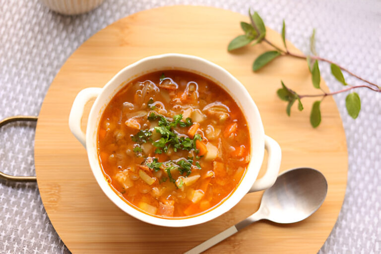 A bowl of colorful vegetable soup garnished with fresh herbs on a wooden serving board.