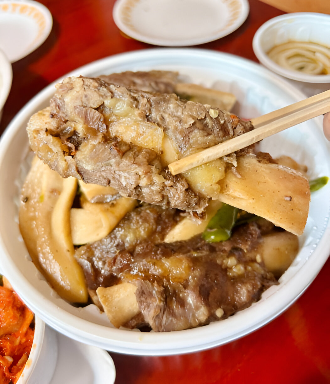 A close-up view of meat and vegetables being picked up with chopsticks from a bowl.