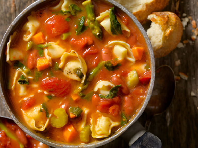 A pot of hearty vegetable soup with pasta on a wooden table, accompanied by chunks of bread.