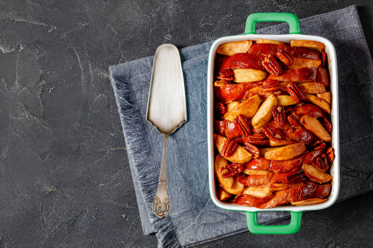 Baking dish filled with sliced apples and pecans on a dark textured background.