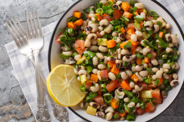 A vibrant salad featuring black-eyed peas, diced tomatoes, bell peppers, and chopped green onions, garnished with a lemon slice.