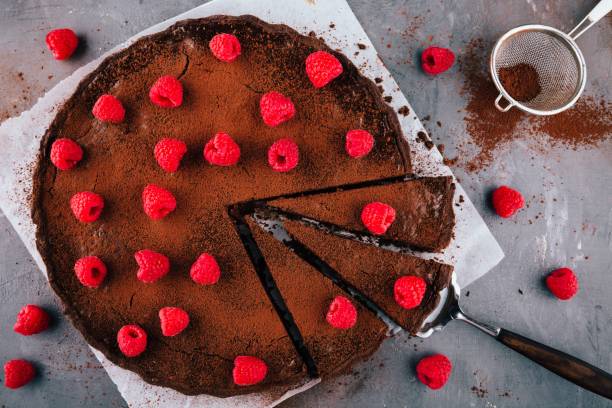 A rich chocolate tart topped with fresh raspberries and cocoa powder, with a slice cut out.