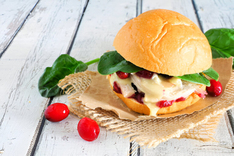 A delicious sandwich with spinach, cranberry sauce, and a creamy filling on a wooden surface.