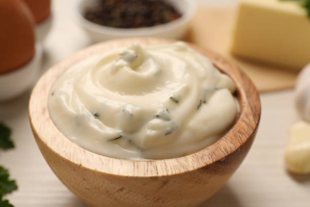 A bowl of creamy mayonnaise with herbs, surrounded by cooking ingredients.