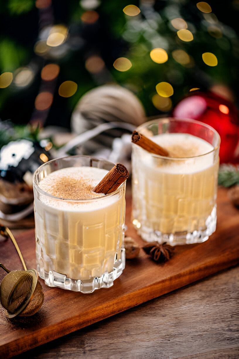 Two cocktails with cinnamon sticks served on a wooden platter, surrounded by festive decorations