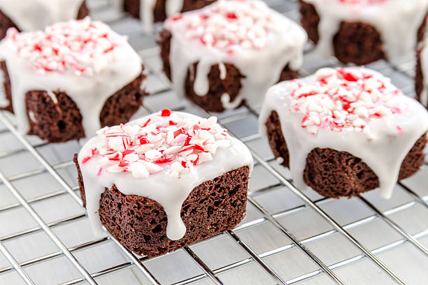 Decadent chocolate brownies topped with white icing and sprinkled with crushed candy canes on a wire rack.