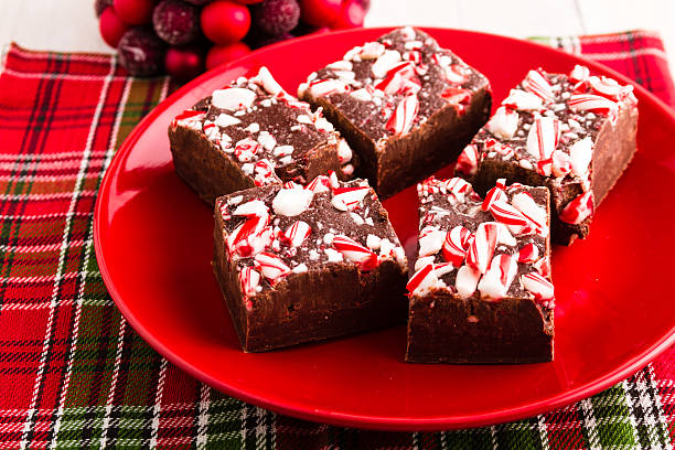 Four pieces of peppermint fudge arranged on a red plate with a festive plaid background.