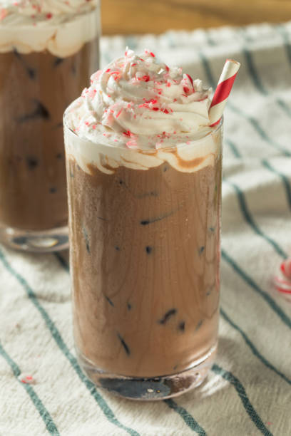 A tall glass of chocolate peppermint drink topped with whipped cream and crushed peppermint candy, with a red and white striped straw.