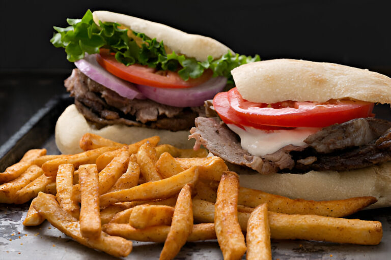 Two delicious sandwiches filled with roast beef, fresh tomatoes, onions, and lettuce, served with golden fries.