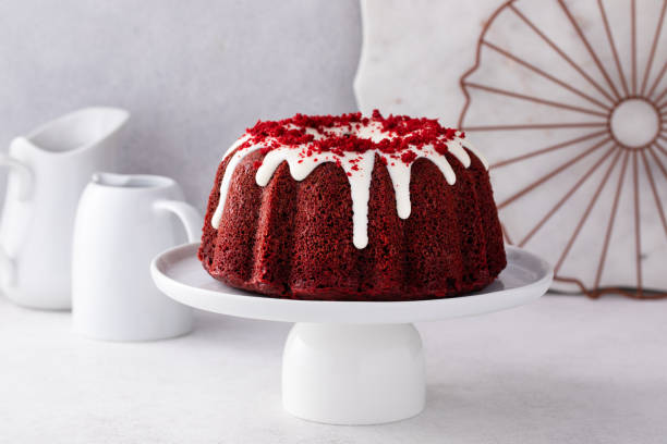 A beautiful red velvet bundt cake with white icing drizzling down, placed on a white cake stand.