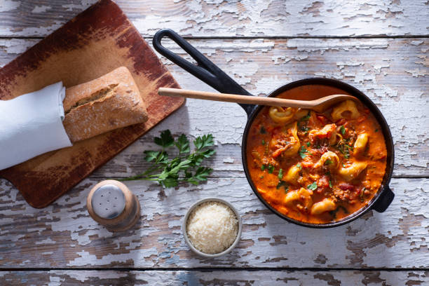 A bowl of tortellini in a rich tomato sauce, with a slice of crusty bread and garnished with parsley on a rustic wooden table.